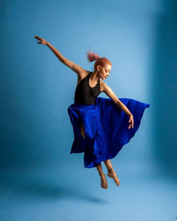 Energetic female dancer leaps gracefully in a studio with a blue background.