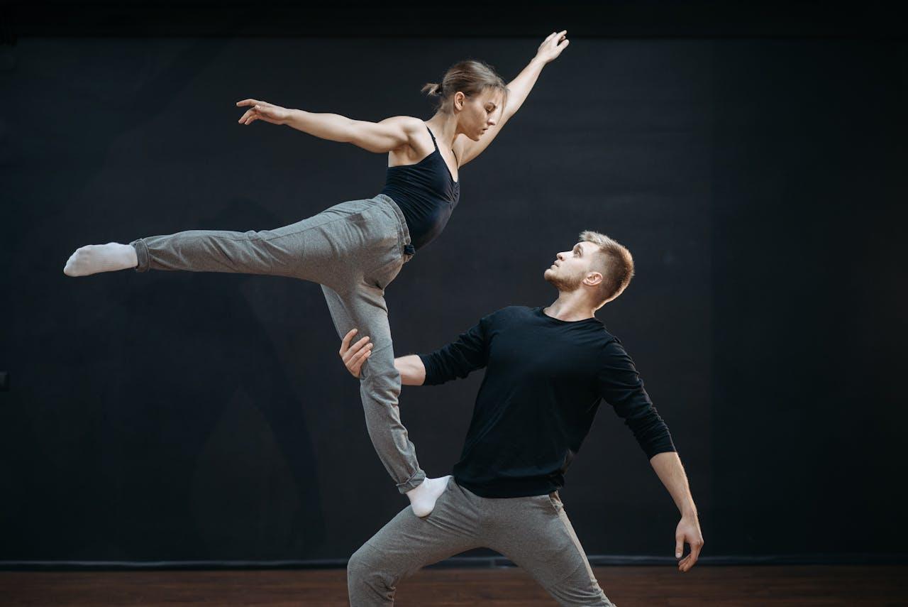 A man and woman perform an elegant contemporary dance lift in a studio setting.