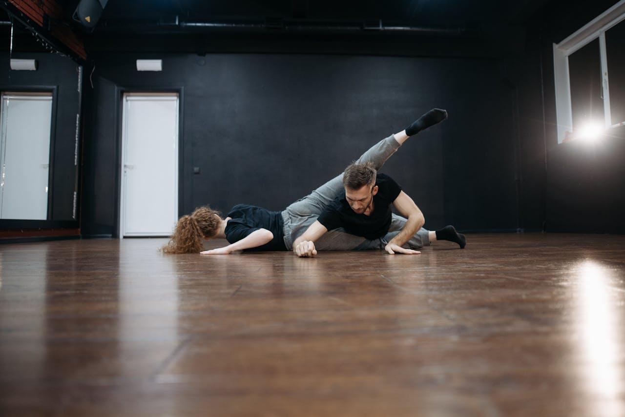 Male and female dancers performing a contemporary routine on a wooden floor in a studio.