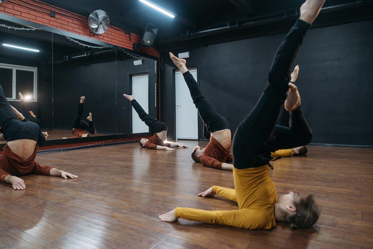 Dancers practicing contemporary moves in a mirrored dance studio with wooden floor.