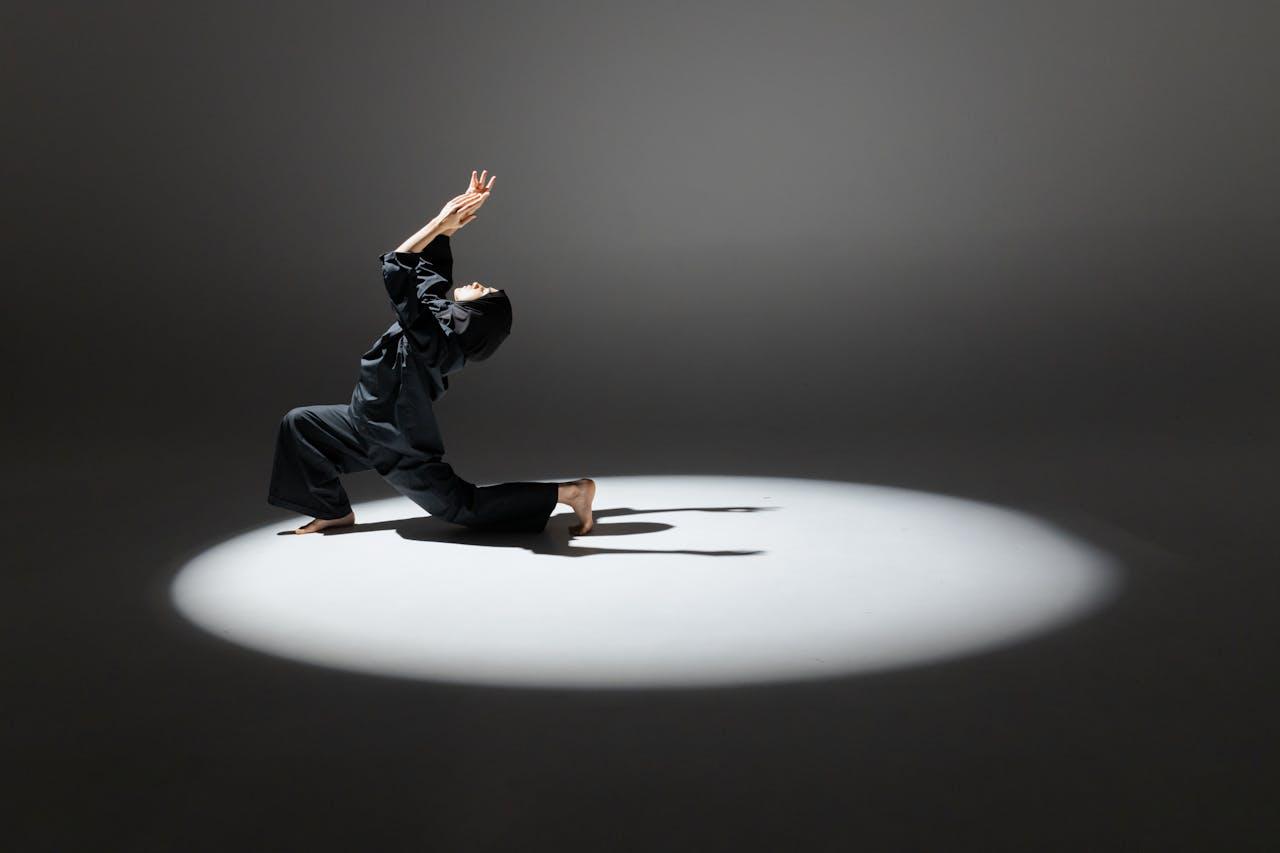 A woman in a hijab performs a contemporary dance pose under dramatic studio lighting.